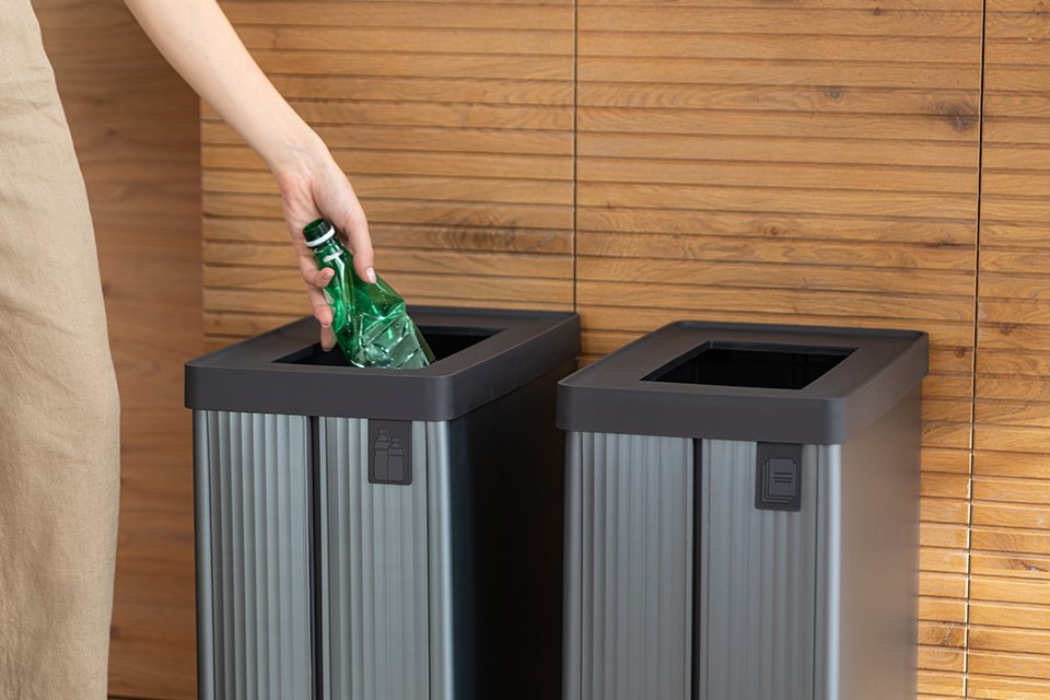 Hand dropping a bottle in Curver Verto recycling bin.